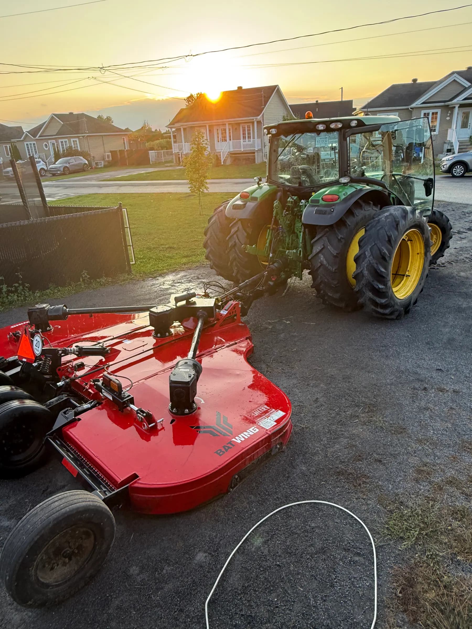 Tracteur John Deere attelé à un gyrobroyeur Batwing rouge au coucher du soleil